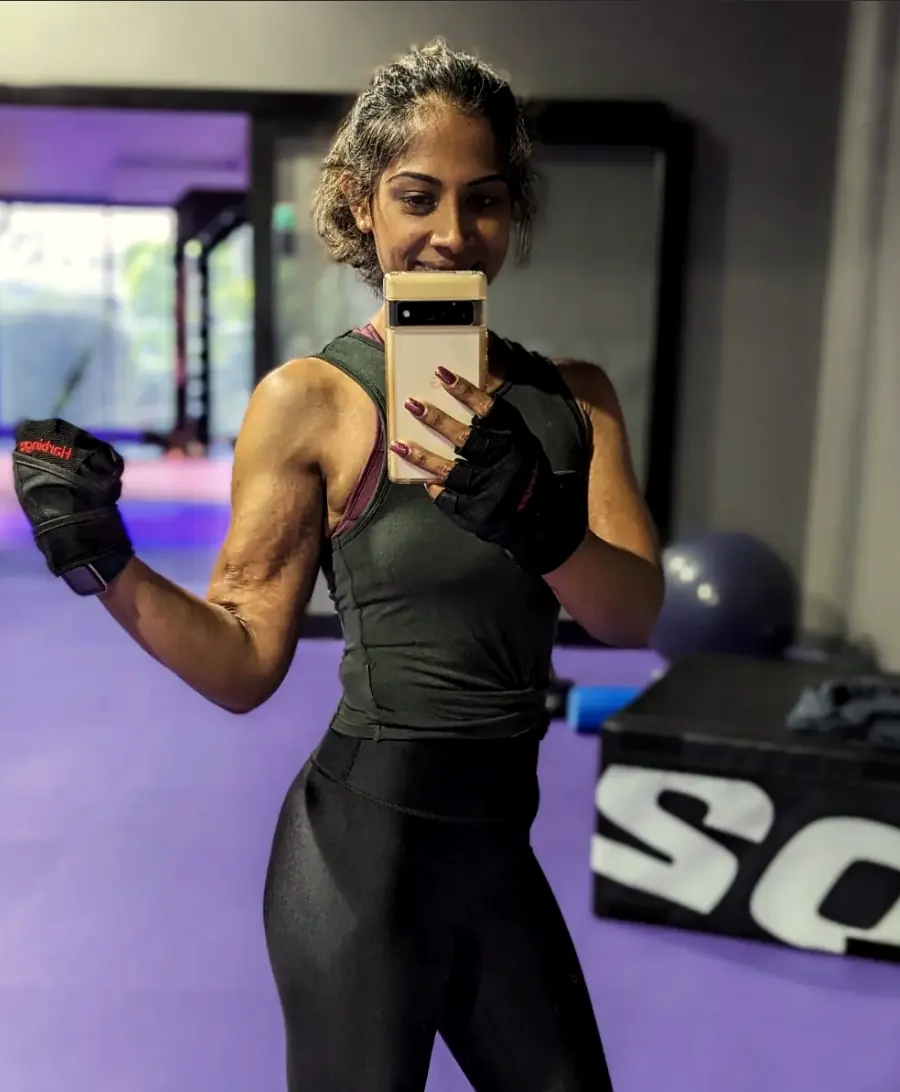 Rose flexing her arm in a gym mirror selfie, wearing lifting gloves and smiling